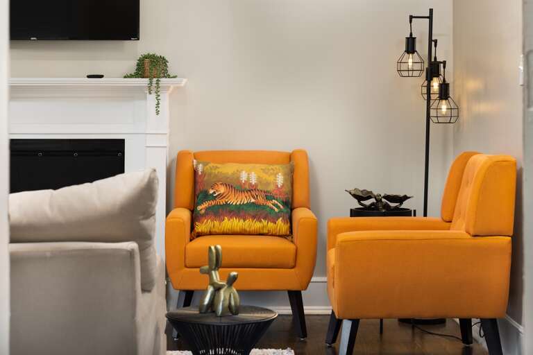 Step into a world of warmth and comfort with our living room's vibrant orange seating, the perfect spot to unwind and enjoy lively conversations or lose yourself in a captivating book. 