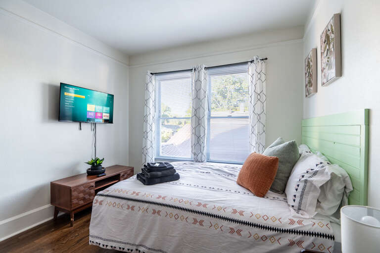 Enjoy a restful night in this cozy bedroom, which includes a queen bed, twin bunkbeds, and a smart TV amidst great natural lighting.