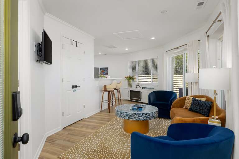 Step into the downstairs living room, a vibrant oasis featuring a cozy faux fireplace, luxurious velvet furniture, and lively colors that spark joy and comfort.