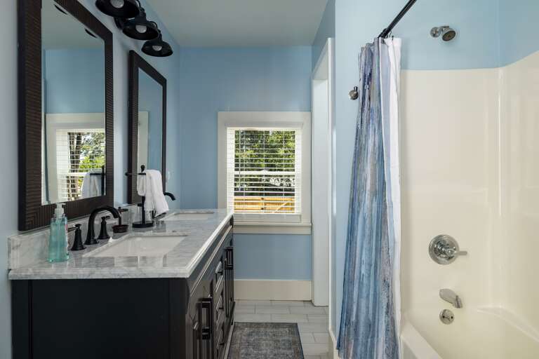 This bathroom features a dual vanity, providing plenty of space for guests to get ready. The modern design and ample lighting add to the room's appeal. 