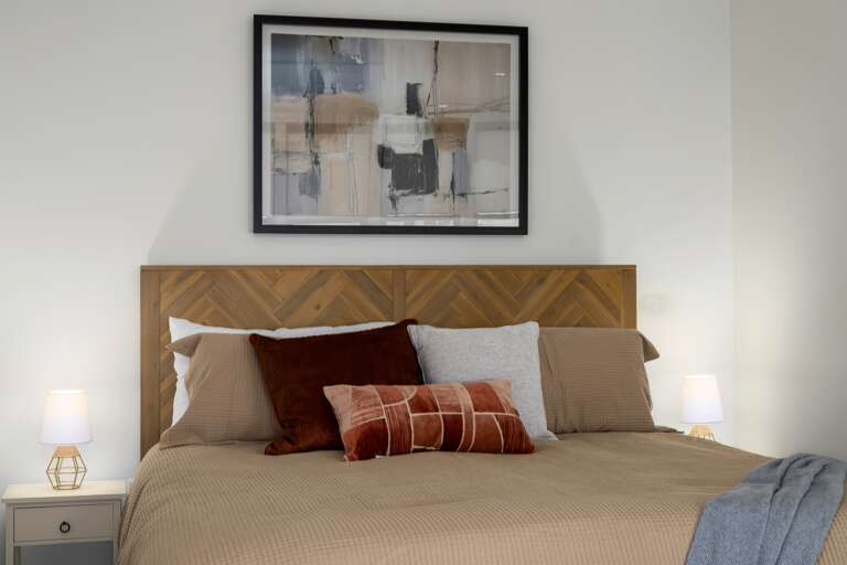 Rest and relaxation—the plush bed with layered pillows and a geometric wooden headboard offers a welcoming, comfortable place to unwind.