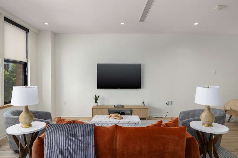 Inviting and modern—the living room showcases a cozy seating arrangement with a plush sofa, armchairs, and soft lighting, all centered around a mounted flat-screen TV for entertainment.