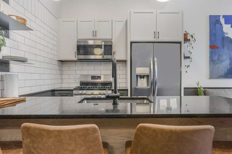 An expansive view of the kitchen showing off its clean design and ample storage, complemented by a subway tile backsplash and a contemporary dining area. An expansive view of the kitchen showing off its clean design and ample storage, complemented by a subway tile backsplash and a contemporary dining area.