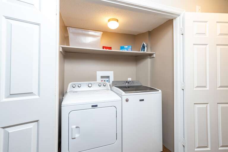 In-unit laundry area with a washer, dryer, and shelving stocked with essentials for guest use.