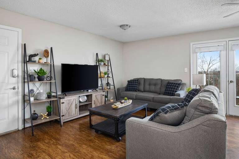 Welcome to Unit F—a living room with a sectional sofa, smart TV, and decorative shelving.