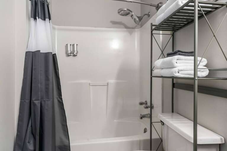 Clean bathroom with a shower/tub combo, storage shelves, and fresh towels for guest convenience.