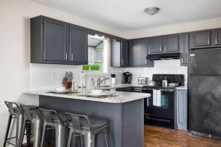 Contemporary kitchen with dark cabinets, granite countertops, and full appliances for cooking convenience. Note: Some of our units have granite countertops others are black. 