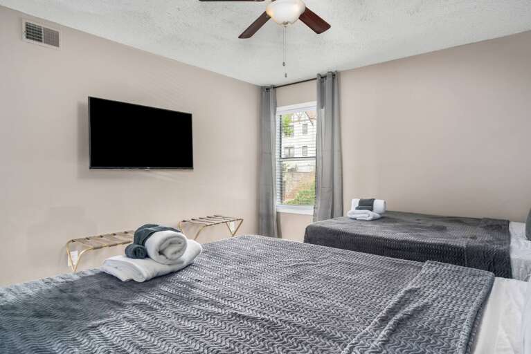 Spacious bedroom with two beds, a mounted flat-screen TV, and large windows.