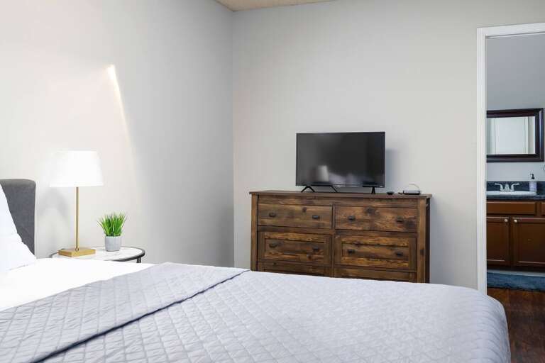 Close-up of the bedroom featuring soft bedding, stylish lighting, and a rustic dresser.