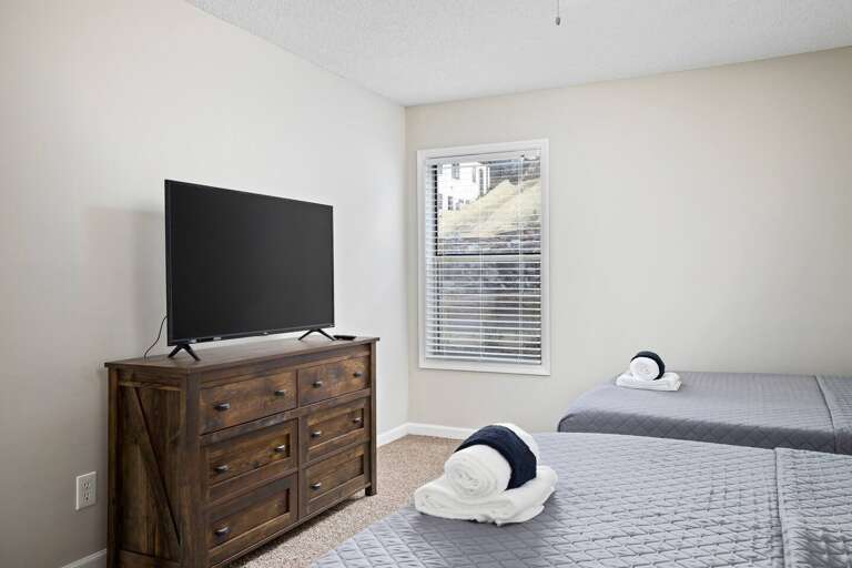 Bedroom featuring a flat-screen TV, rustic wooden dresser, and natural light through the window.