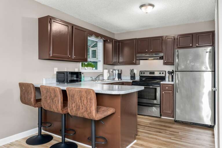 Fully equipped kitchen with stainless steel appliances, bar seating, and dark cabinetry.