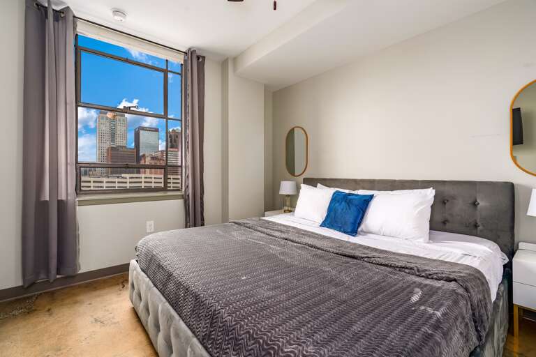 Elegant bedroom featuring a king-size bed and large windows showcasing city views.