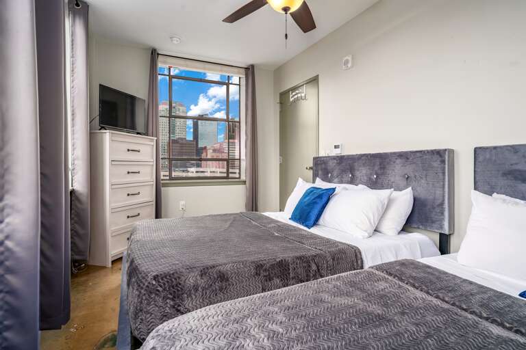 Stylish bedroom with two queen beds, large windows, fresh linens, and vibrant accent pillows.