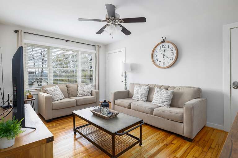 The spacious living room features comfortable seating, large windows for natural light, and a modern farmhouse aesthetic.