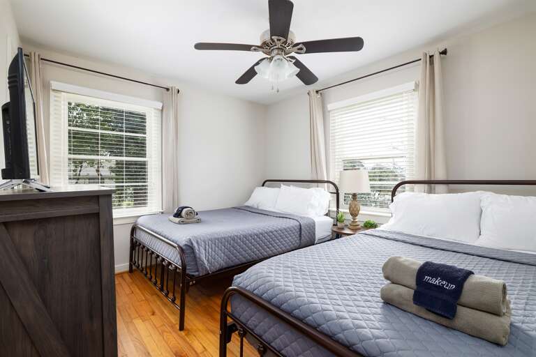 A cozy bedroom featuring two queen beds, soft gray bedding, and large windows for plenty of natural light. A cozy bedroom featuring two queen beds, soft gray bedding, and large windows for plenty of natural light.