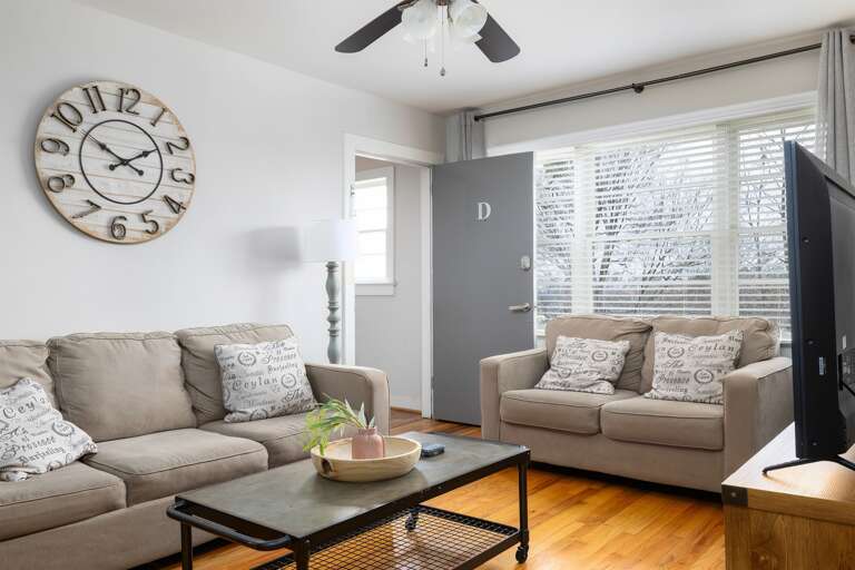 Bright and airy living room in Unit D, featuring comfortable seating, a farmhouse clock, and large windows for natural light. Bright and airy living room in Unit D, featuring comfortable seating, a farmhouse clock, and large windows for natural light.