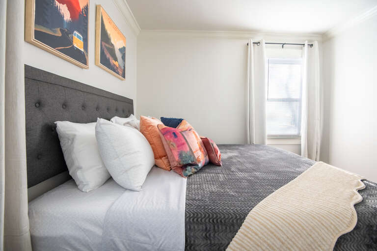 Side view of the bright king bedroom with stylish pillows, perfect lighting, and modern simplicity.