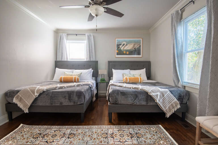 Another view of the double queen bedroom showing soft gray bedding, natural light, and calming decor.