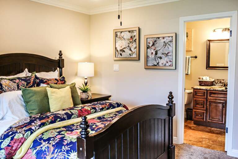 Bedroom With Bed, Patterned Bedding, Pendant Light, And Open Door To Bathroom