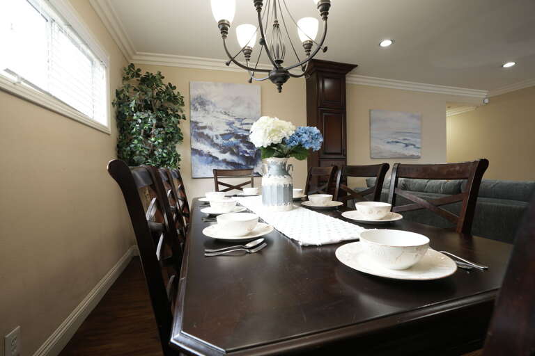 Dining Room With Dark Wood Table Set For Dinner, Sea Scene Painting, Chandelier Above