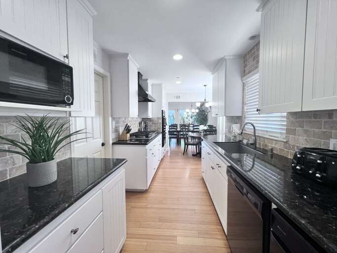 Bright, White Kitchen With Black Countertops Leading To Dining Area
