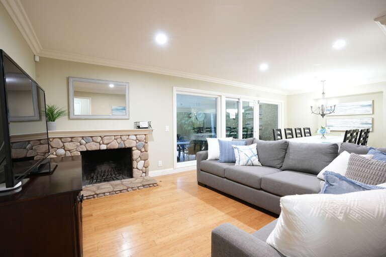 Spacious Living Space With Sleek Sofas, Stone Fireplace, And Sliding Glass Doors Leading To Outdoor View