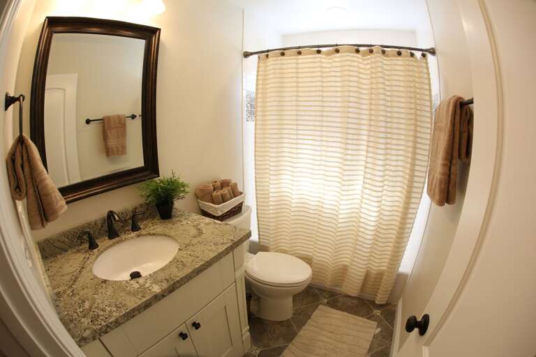 Bright Bathroom With Beige Curtain, Rounded Mirror, And Tiled Floor In Vacation Rental Bright Bathroom With Beige Curtain, Rounded Mirror, And Tiled Floor In Vacation Rental
