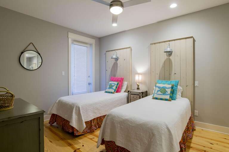 Twin beds with white quilted coverlets and colorful sea turtle pillows stand against pale wood headboards.