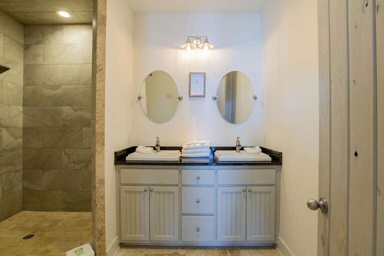 Twin oval mirrors hang above a black granite countertop with white square sinks and silver faucets.