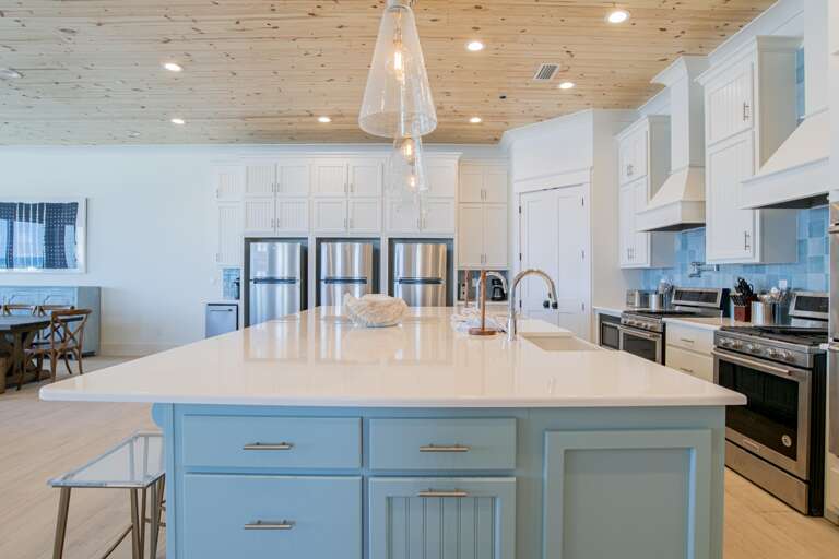 Kitchen island with pale blue cabinetry and white quartz countertop under cone-shaped glass pendant lights.