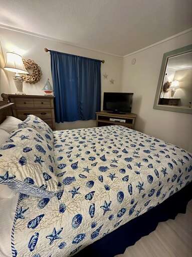 Unwind in this ocean-inspired bedroom featuring seashell bedding, soft lighting, and a flat-screen TV for relaxed coastal evenings. Unwind in this ocean-inspired bedroom featuring seashell bedding, soft lighting, and a flat-screen TV for relaxed coastal evenings.