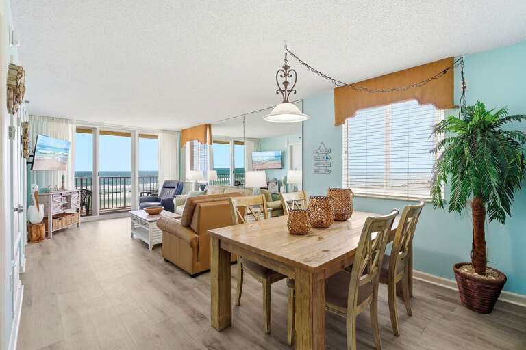 Bright beachfront condo featuring open living and dining area, ocean-view balcony, and coastal decor. Enjoy your beach stay with relaxing seating, natural light, and direct views of the shoreline.