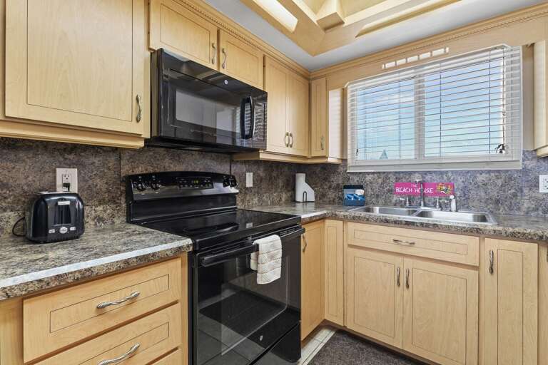 Kitchen Corner Capture Featuring Beige Cabinetry And Black Appliances Beneath Bright Blinds