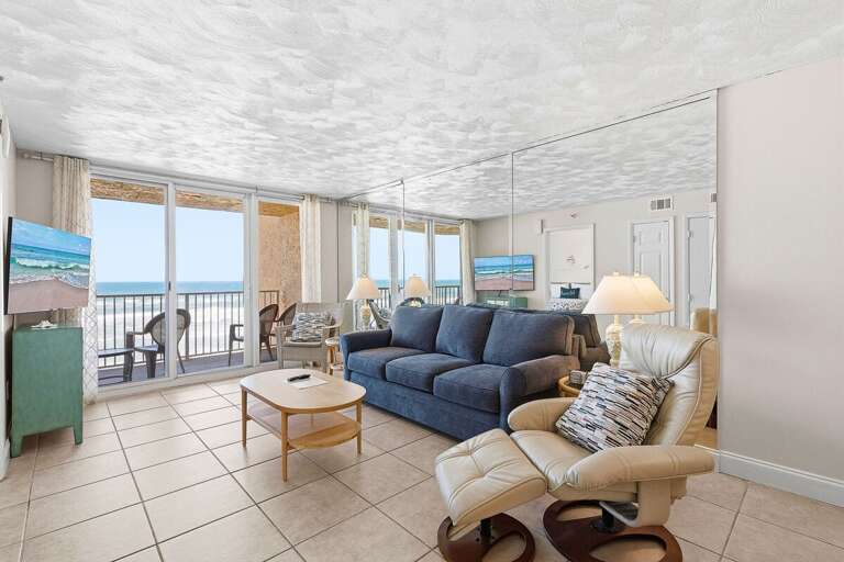 Relax in this inviting beach stay living room with comfortable seating, large windows, and direct access to an oceanfront balcony. Enjoy stunning views and unwind after a day on the sandy shores.