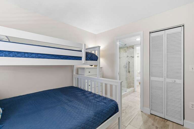 This beach stay bunk room offers comfortable sleeping for guests with convenient access to a nearby bathroom. Perfect for families or groups looking to relax and recharge after a day at the beach.