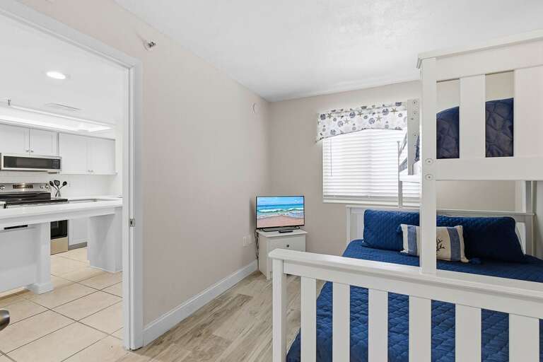 This beach stay bunk room offers cozy sleeping space with a TV and easy access to the kitchen and living areas. Perfect for families or groups looking to relax after a fun-filled day at the beach.