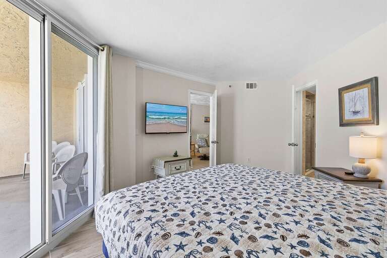 Unwind in this comfortable beach stay bedroom featuring a cozy bed, TV, and direct access to a private balcony. Enjoy fresh coastal air and easy access to living spaces for a perfect seaside getaway.