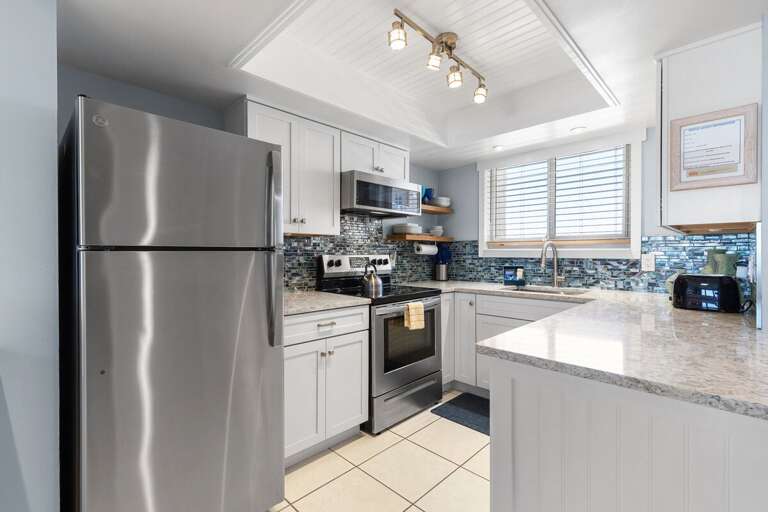 Stainless Steel Fridge In Stone-speckled Kitchen With White Cabinets And Window