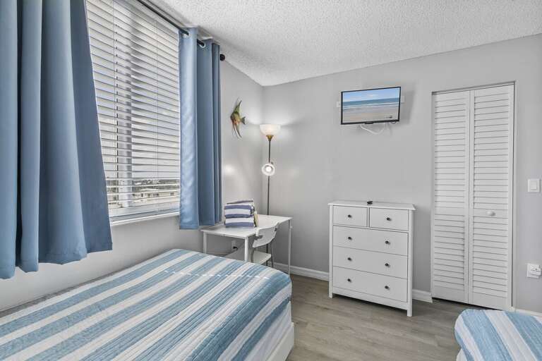 This cozy twin bedroom features a soothing coastal-inspired design with soft blue and white striped bedding and matching curtains that frame large windows, filling the room with natural light. This cozy twin bedroom features a soothing coastal-inspired design with soft blue and white striped bedding and matching curtains that frame large windows, filling the room with natural light.
