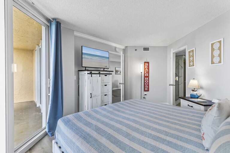 The soft blue and white striped bedding enhances the coastal theme, accompanied by beach-inspired wall decor and a rustic white dresser topped with a flat-screen TV. The soft blue and white striped bedding enhances the coastal theme, accompanied by beach-inspired wall decor and a rustic white dresser topped with a flat-screen TV.