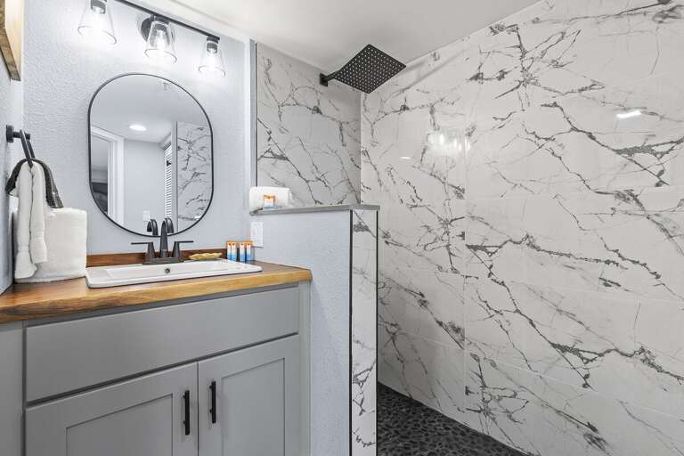 A beautifully designed bathroom featuring marble walls, a rain shower, sleek vanity with wood countertop, and contemporary lighting, perfect for a luxurious and stylish retreat.