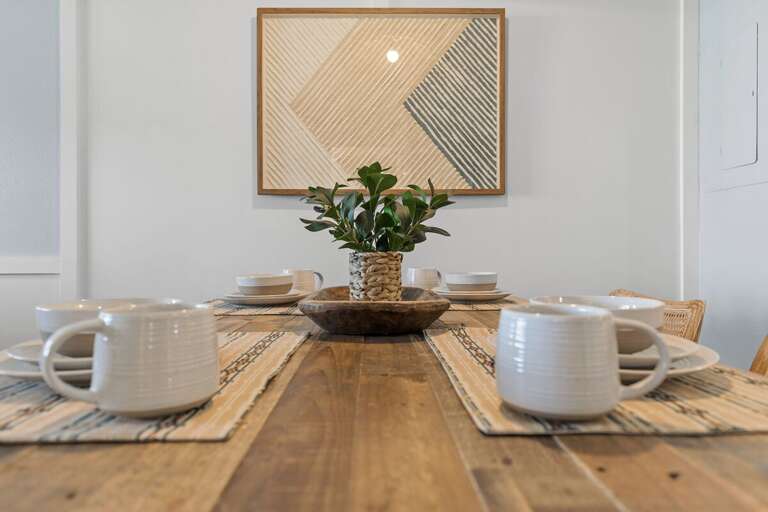 A beautifully set dining table features rustic wood, simple dishware, and a natural centerpiece. The