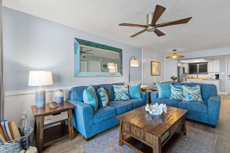 This cozy living room features vibrant blue sofas, colorful throw pillows, and a rustic wood coffee
