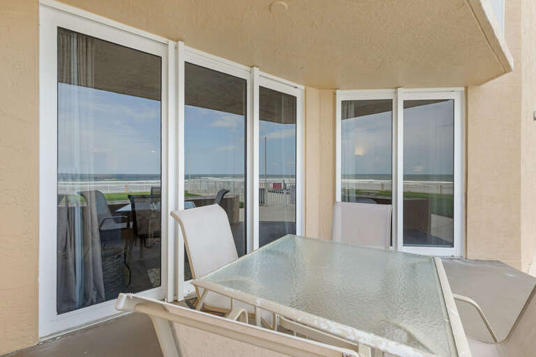 A cozy oceanfront patio featuring a glass-top table and seating, perfect for outdoor dining or