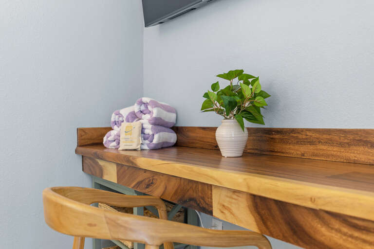 A cozy workspace adorned with fresh greenery and soft towels, perfect for a peaceful environment. The wooden desk brings warmth and nature-inspired aesthetics to this corner.