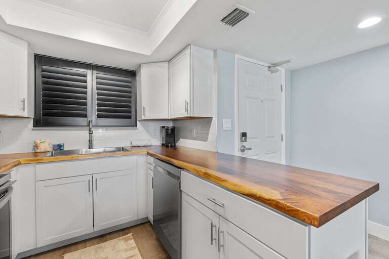 This modern kitchen boasts a beautiful wooden countertop, sleek white cabinetry, and a large sink