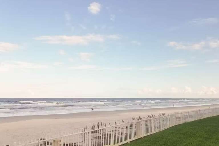 A peaceful stretch of sandy beach meets gentle waves under a clear sky, offering a perfect spot for a quiet stroll or simply enjoying the beauty of the ocean horizon.