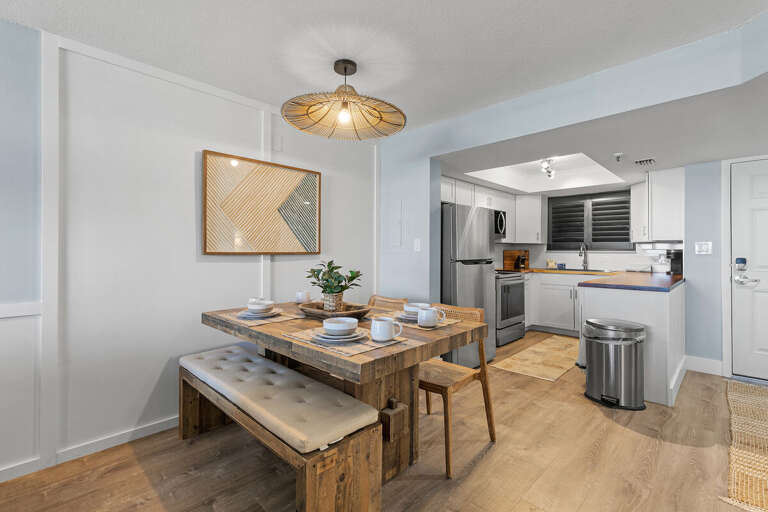A rustic dining table with bench seating complements the modern kitchen's stainless steel appliances, creating a warm and inviting space perfect for casual meals and gatherings.