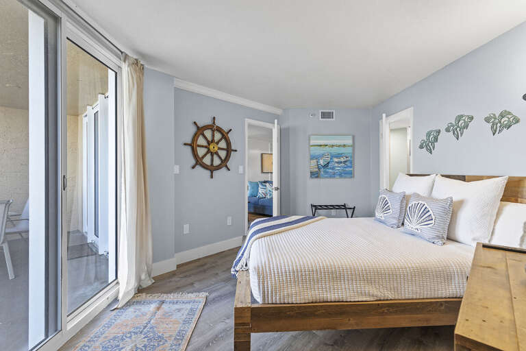 This serene bedroom features coastal decor, including a ship's wheel and ocean-themed artwork, with sliding door access to the patio for a relaxing indoor-outdoor experience.