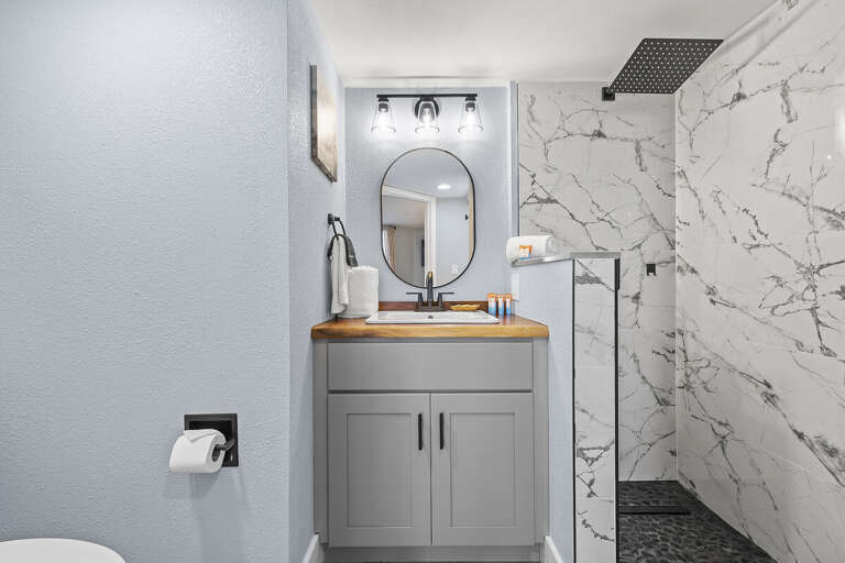 A sleek bathroom featuring a marble-tiled shower, modern vanity with wood accents, and stylish lighting, offering a clean and refreshing space with contemporary design